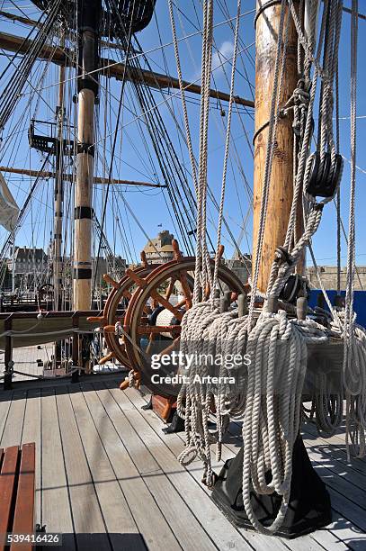 Steering wheel and ropes coiled around belaying pins aboard the Grand Turk / Etoile du Roy, a three-masted sixth-rate frigate replica of HMS...