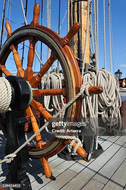 Steering wheel and ropes coiled around belaying pins aboard the Grand Turk / Etoile du Roy, a three-masted sixth-rate frigate replica of HMS...