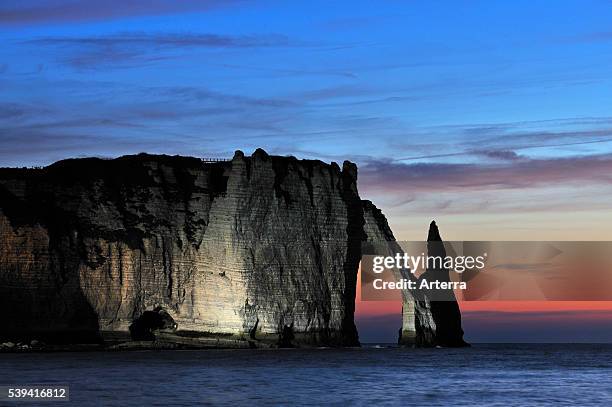 Aiguille and The Porte d'Aval at sunset, a natural arch at Etretat which is illuminated artificially, Normandy, France.