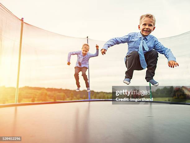 jüngeren brüder tragen anzug springen auf trampolin - trampoline stock-fotos und bilder