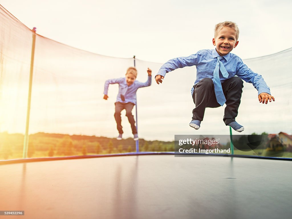 Little brothers wearing suits jumping on trampoline