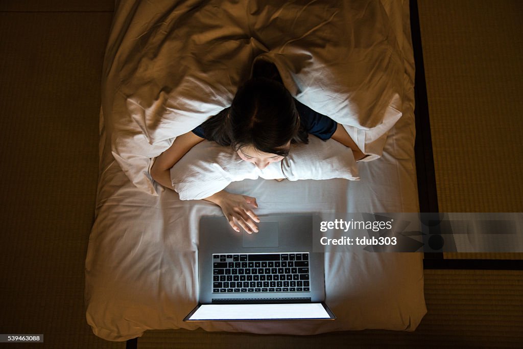 Woman using a laptop computer while laying on Japanese futon