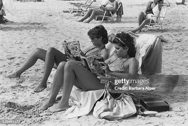 Two young women reading 'Glamour' magazine on the beach in Atlantic City, New Jersey, 31st July 1983.