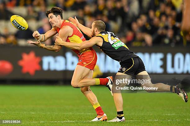 Jesse Lonergan of the Suns handballs whilst being tackled by Kane Lambert of the Tigers during the round 12 AFL match between the Richmond Tigers and...