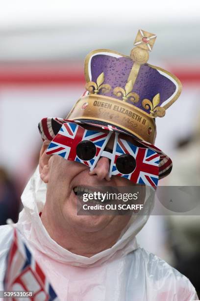 Man wears a pair of Union flag glasses and a paper crown as he joins members of the public braving the inclement weather to watch events on a large...