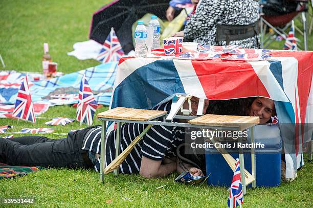 Gisella Rusca and Art Fleischmann shelter under a picnic table during heavy rain in Green Park as members of the public watch The Queen's Patronage...