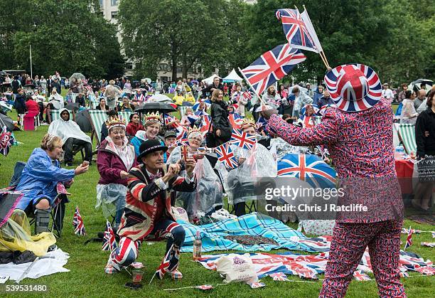 Joseph Afrane in Union Jack clothing waves flags as members of the public in Green Park gather for a picnic and watch The Queen's Patronage on a big...