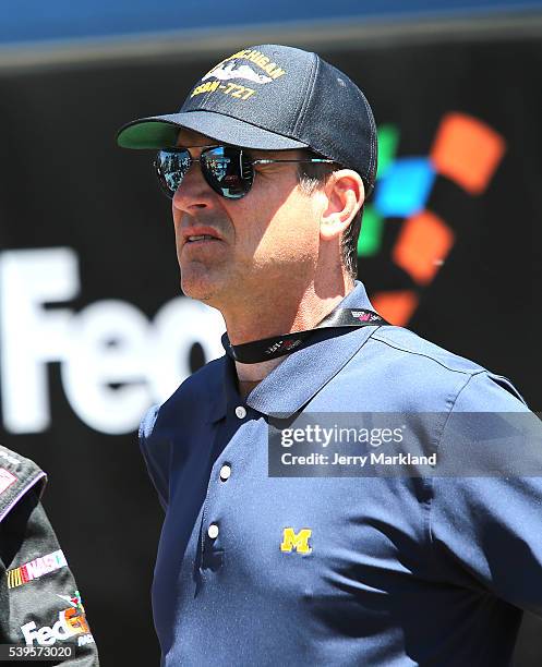 University Of Michigan football coach Jim Harbaugh stands on pit road during the NASCAR Sprint Cup Series FireKeepers Casino 400 at Michigan...