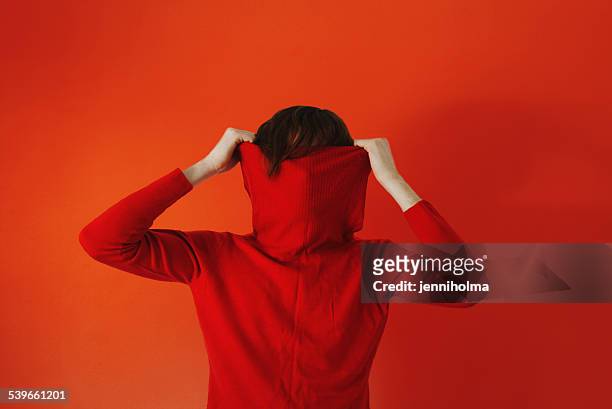 man pulling red sweater over face against red background - mock turtleneck stock-fotos und bilder