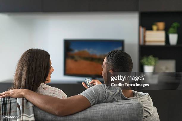 usa, new jersey, couple sitting in living room and watching tv - african watching tv foto e immagini stock