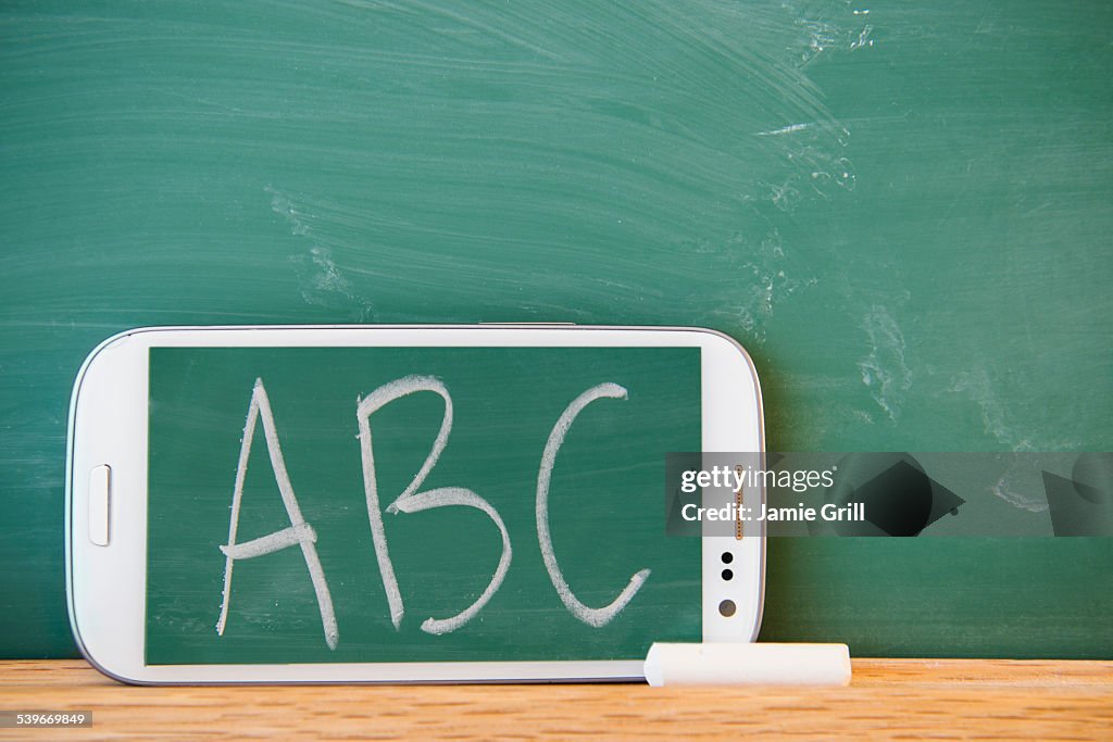 Smartphone leaning against chalkboard with ABC letters displayed