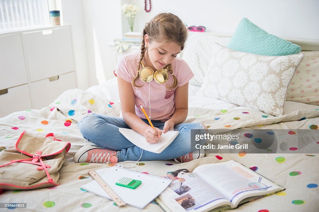 USA, New Jersey, Girl (12-13) sitting on bed doing homework