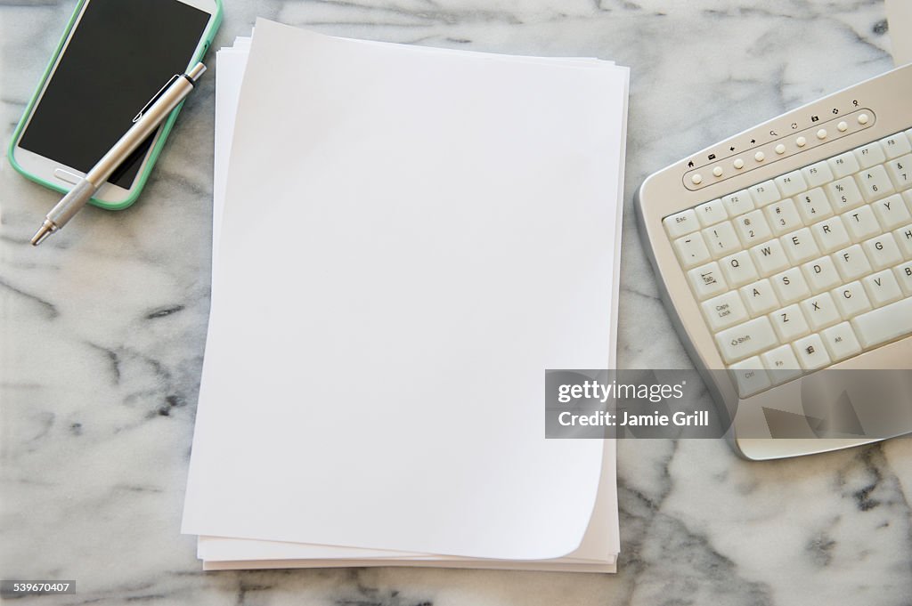 Studio shot of smart phone, sheets of paper, pen and computer keyboard