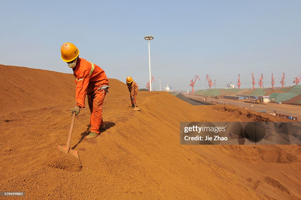 Workers shovel iron ore from Australia while it is being offloaded at Rizhao Port