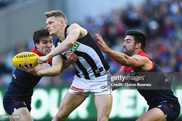 Adam Treloar of the Magpies handballs whilst being tackled by Jack Viney and Chris Dawes of the Demons during the round 12 AFL match between the...