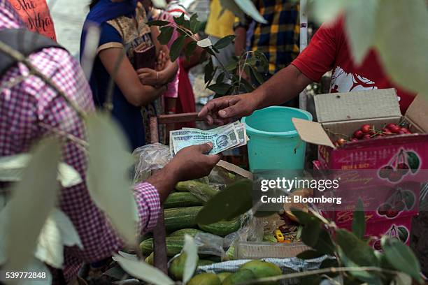 Customer hands over Indian rupee banknotes to a vendor at a fruit and vegetable market stall in the McLeod Ganj area of Dharamsala, India, on...