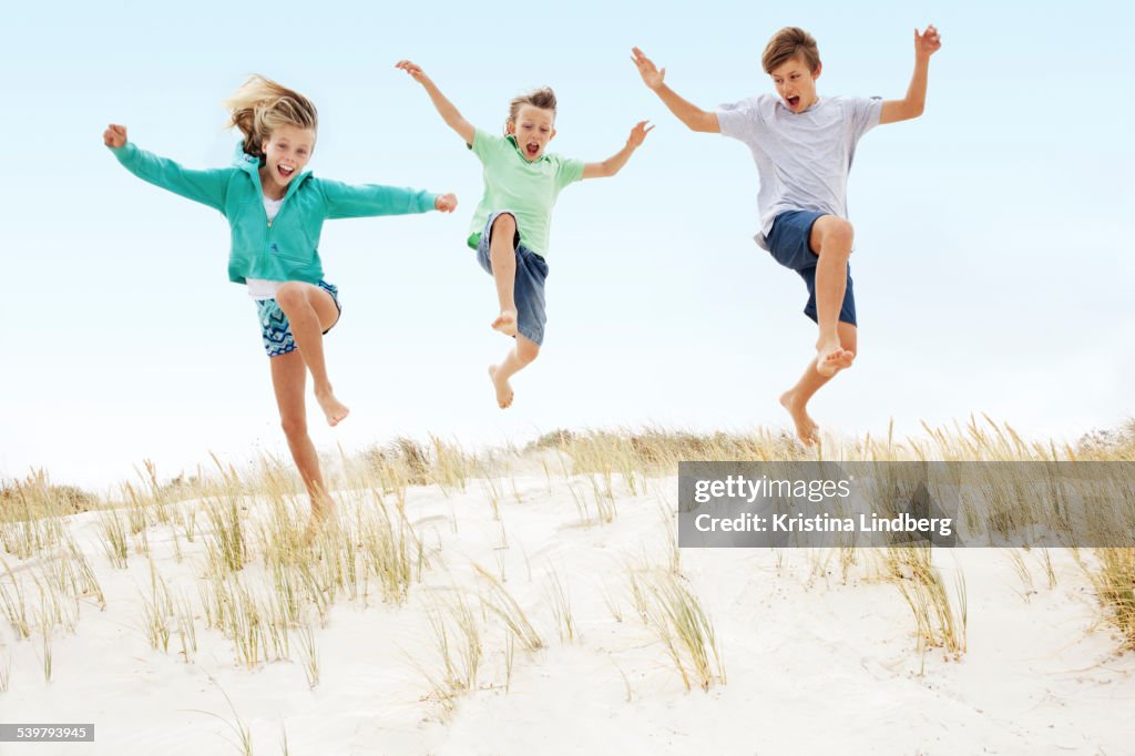 Three kids running and jumping off a sand dune.