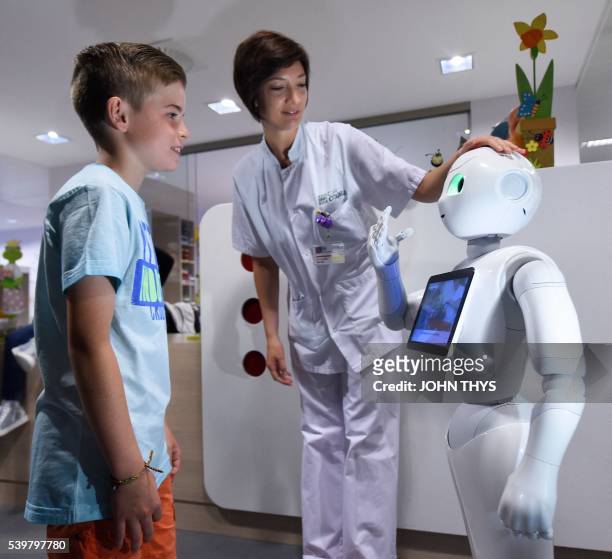 Young boy talks with the robot Pepper next to a nurse during a press conference on June 13, 2016 at the CHR Citadel hospital centers of Liege. - the...