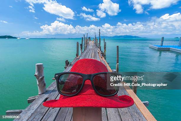sea and summer concept,sunglasses above red hat and wood bridge on the sea - blue white summer hat background stock pictures, royalty-free photos & images