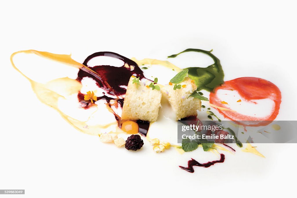 Cake slices garnished with spilled sauces and berries against white background