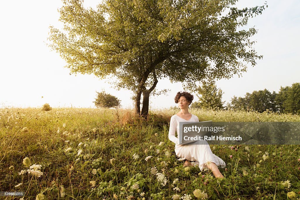 Woman with laptop relaxing on field