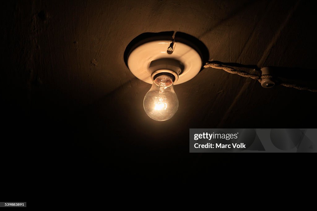 Low angle view of lit light bulb on ceiling