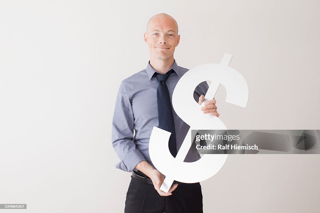 Portrait of confident businessman holding dollar sign against white background