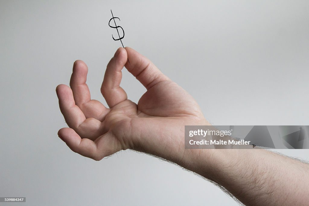 Cropped image of mans hand holding dollar sign against gray background