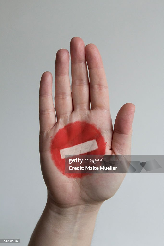 Close-up of stop sign painted on mans hand against gray background