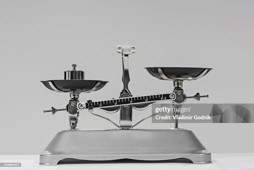 Old-fashioned weight on weighing scale against gray background