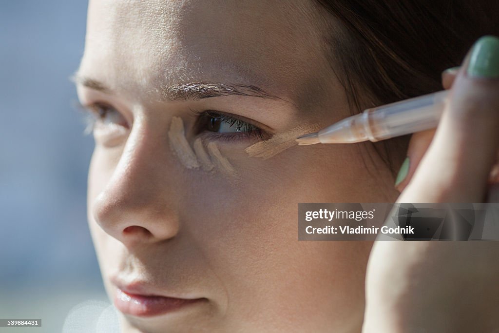 Close-up of young woman applying make-up foundation outdoors