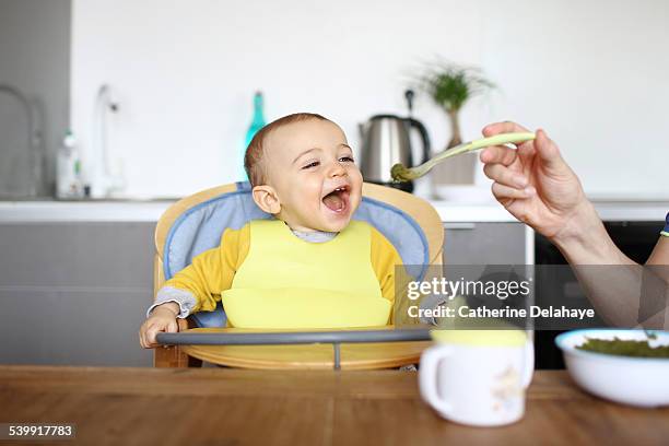 a 1 year old baby boy eating in his high chair - baby eat stock-fotos und bilder