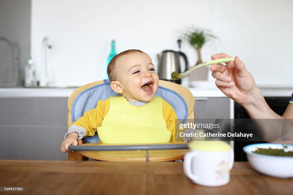 A 1 year old baby boy eating in his high chair