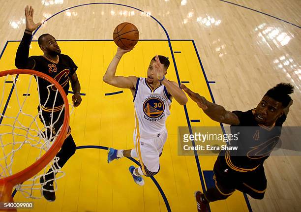 Stephen Curry of the Golden State Warriors goes up for a shot between LeBron James and Iman Shumpert of the Cleveland Cavaliers in the first half in...