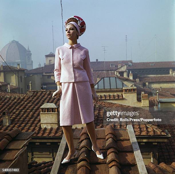 Sixties Fashion - A young female model wears a tailored frock suit in pink wool and matching foulard hat, with the line of the frock slightly...