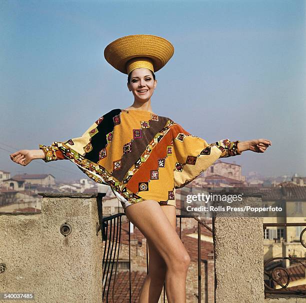 Sixties Fashion - A young female model wears a beach outfit in shades of orange, yellow and brown in a diagonal pattern, the hip hugging tunic having...