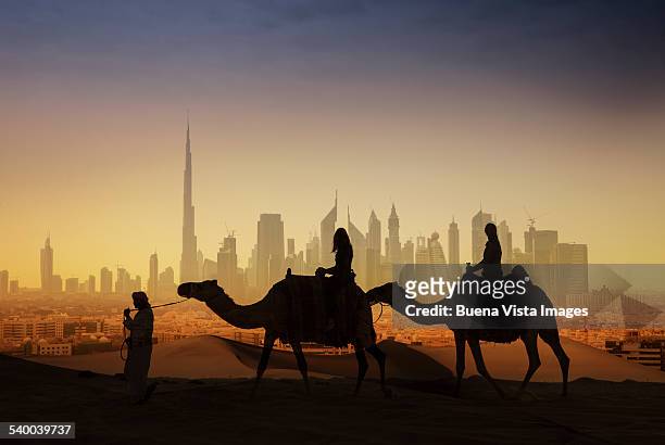 tourists on camels watching a futuristic city - dubai stock-fotos und bilder