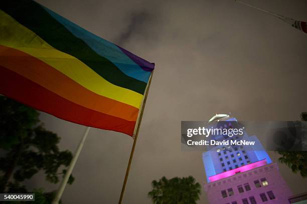 Woman waves a flag near City Hall, which is lit in the colors of the rainbow flag to honor the LGBT victims of the worst mass shooing in United...