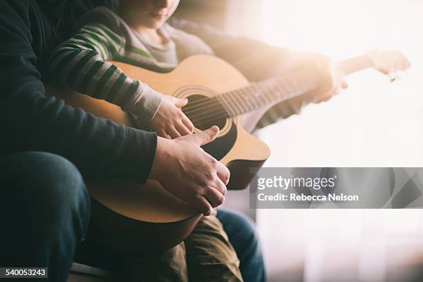father teaching his son to play guitar - kids instruments stock-fotos und bilder