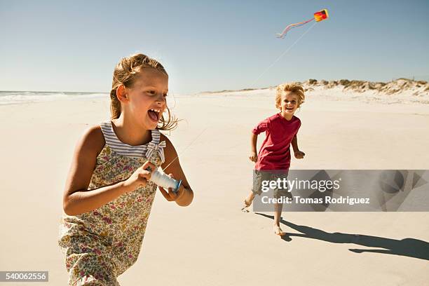 boy (6-7) and girl (8-9) flying kite on sandy beach - drachenfliegen stock-fotos und bilder