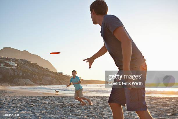 father with son (7-9) playing frisbee on beach - frisbee fotografías e imágenes de stock