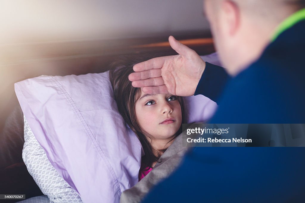 Father checking daughter's forehead for fever