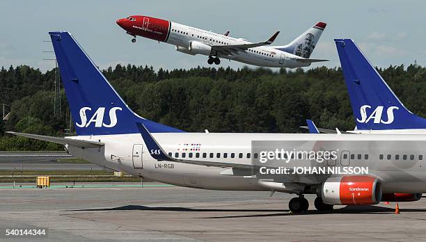 Norwegian Boeing 737-800 takes off behind the tails of two of Scandinavian airline Boeing 737 aircrafts parked at Terminal 4 during the SAS pilots?...