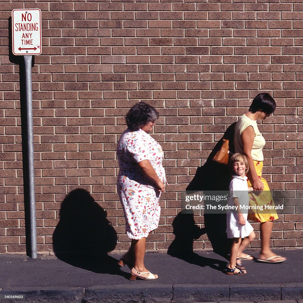 A grandmother, mother and daughter walk past a 'no standing' sign on the footpat