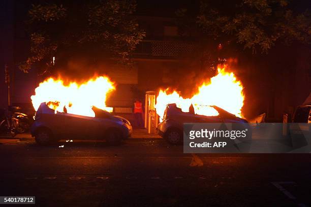 Photo taken on June 14, 2016 shows two Autolibs on fire in a street of Paris after been burnt by a group of hooded people. / AFP / Samantha DUBOIS