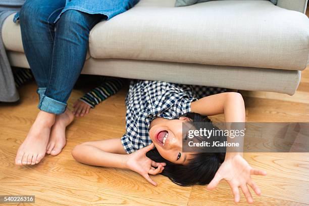young girl crawling out from under the sofa - under sofa stockfoto's en -beelden