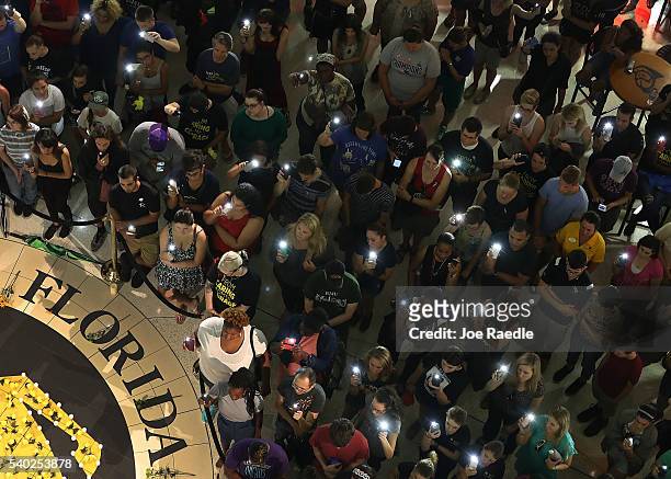 People hold up their cellphones instead of candles as names of those killed are read aloud during a memorial service at the University of Central...