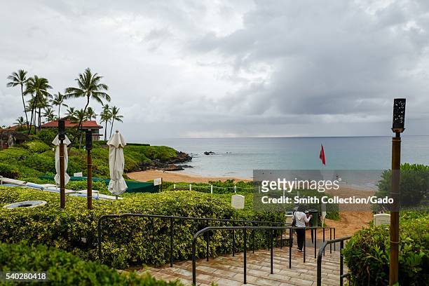 Rainy and overcast day at Wailea Beach, viewed from the terrace of the Four Seasons Resort Maui at Wailea, with tourists walking towards the beach...