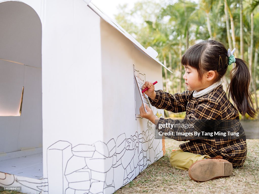 Lovely girl painting on a cardboard playhouse