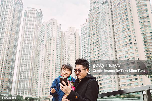 young dad using smartphone joyfully with daughter - chinese family with one child stock pictures, royalty-free photos & images